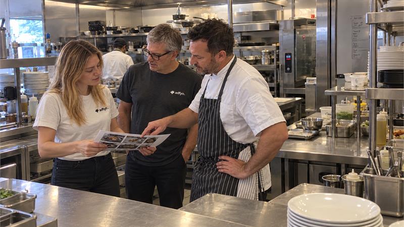 The Adfyo team reviewing food story photographs with a chef at a working restaurant kitchen pass