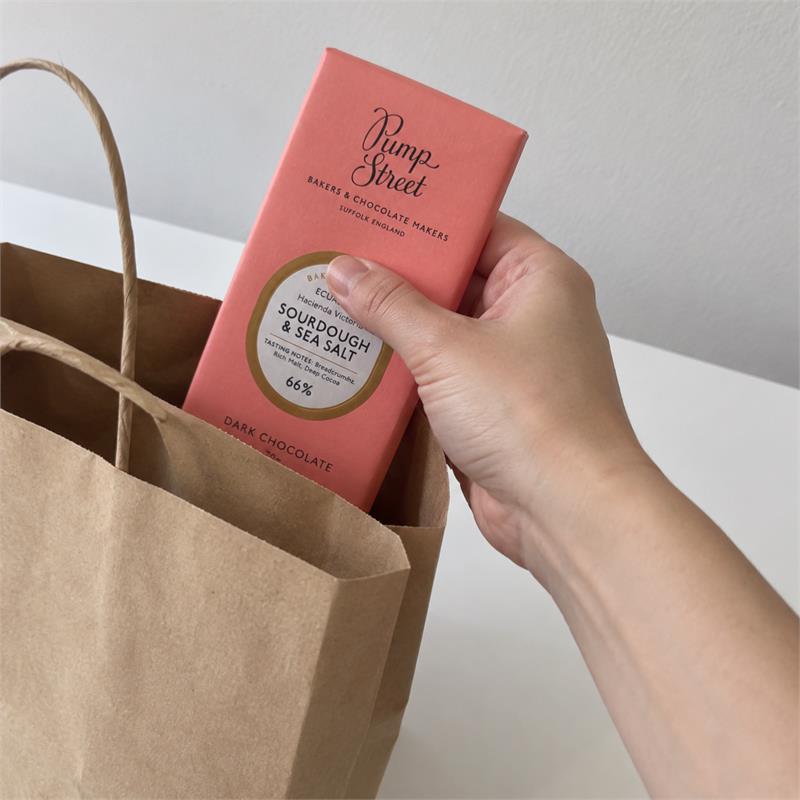 A hand holding a wrapped Pump Street Sourdough and Sea Salt chocolate bar above a shopping bag